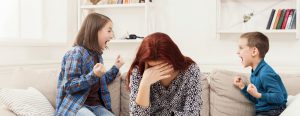 אמא יושבת מחזיקה את ראשה מאחריה שני אחים מתווכחים-הדרכה לבעיות התנהגות
