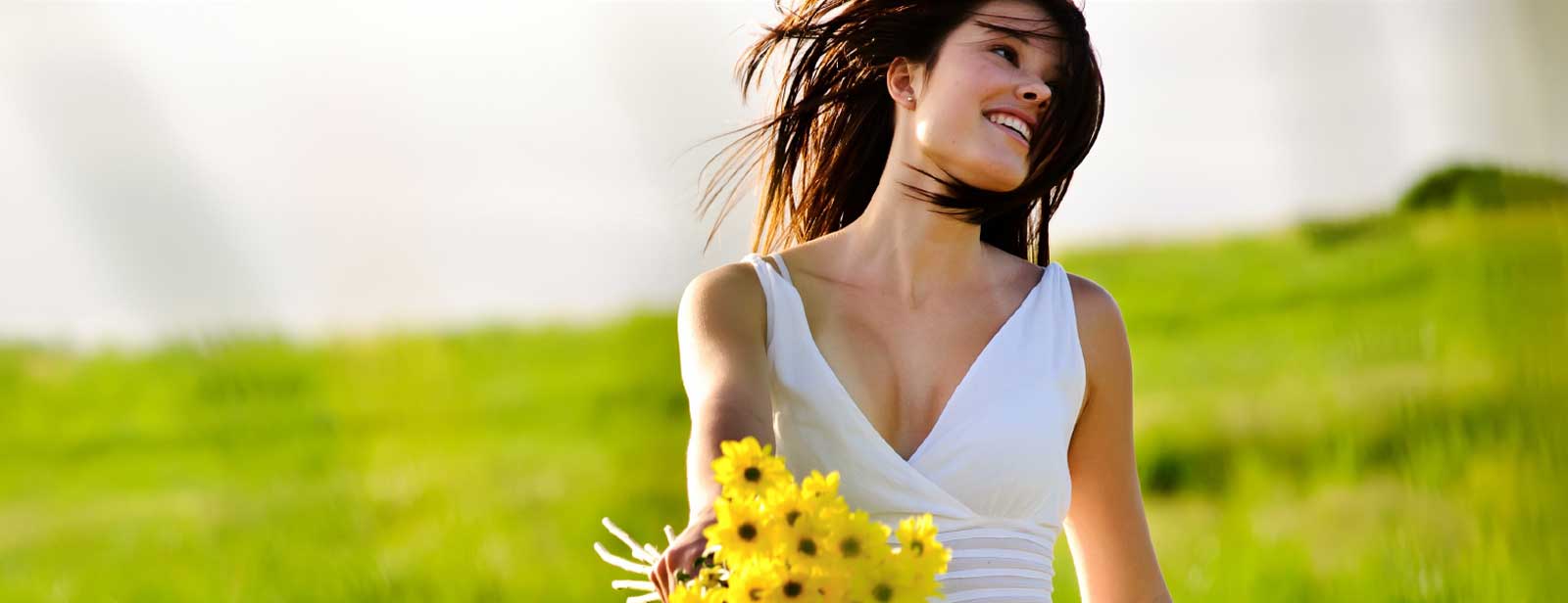 אישה בלבן מחזיקה סביונים בשדה-העצמה עצמית