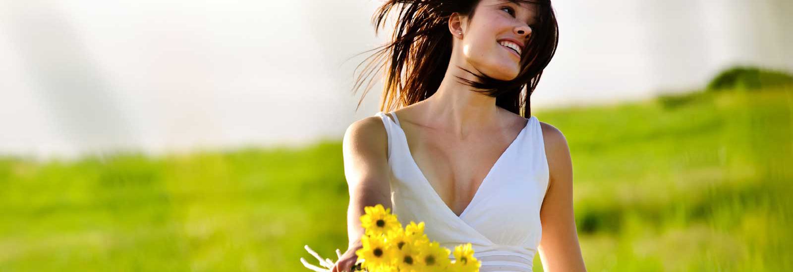 אישה בלבן מחזיקה סביונים בשדה-העצמה עצמית